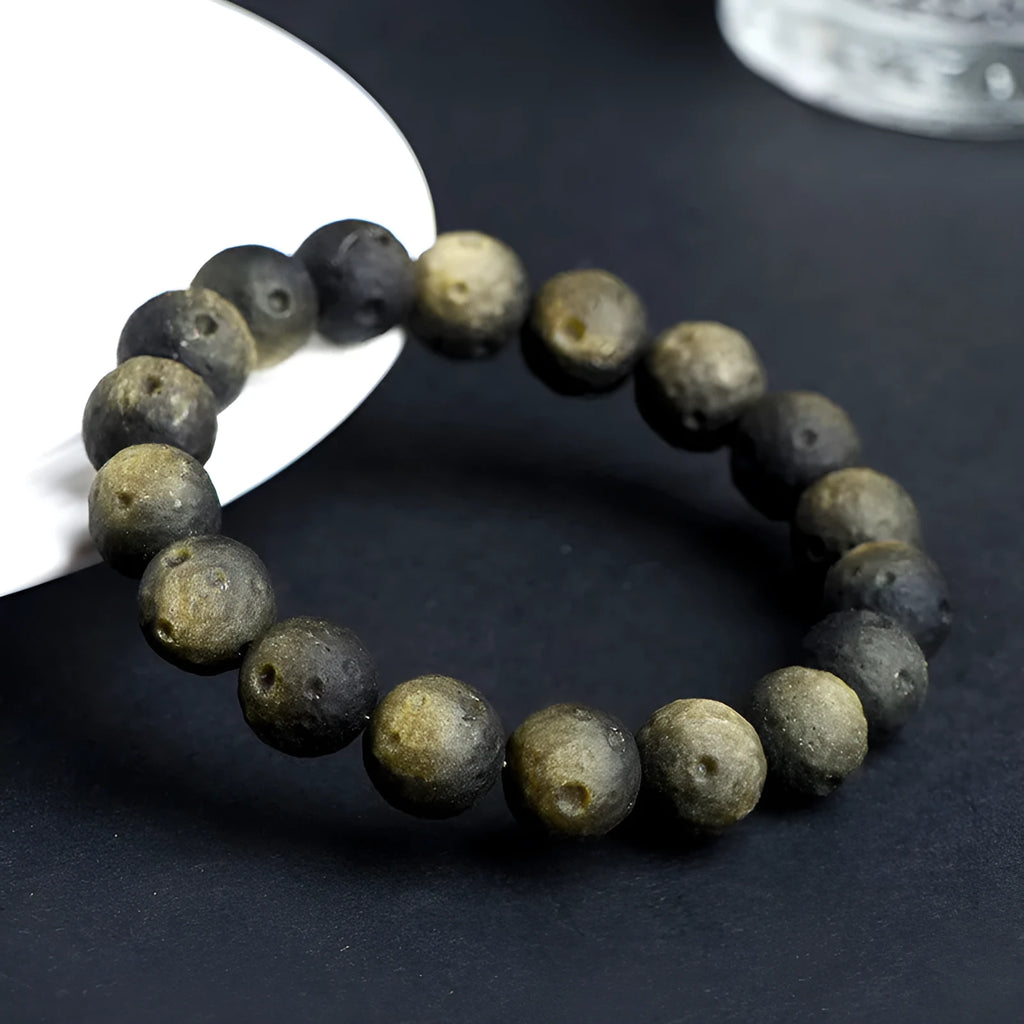 Natural obsidian crater ball bracelet with meteorite-like texture in silver stone or gold finish.