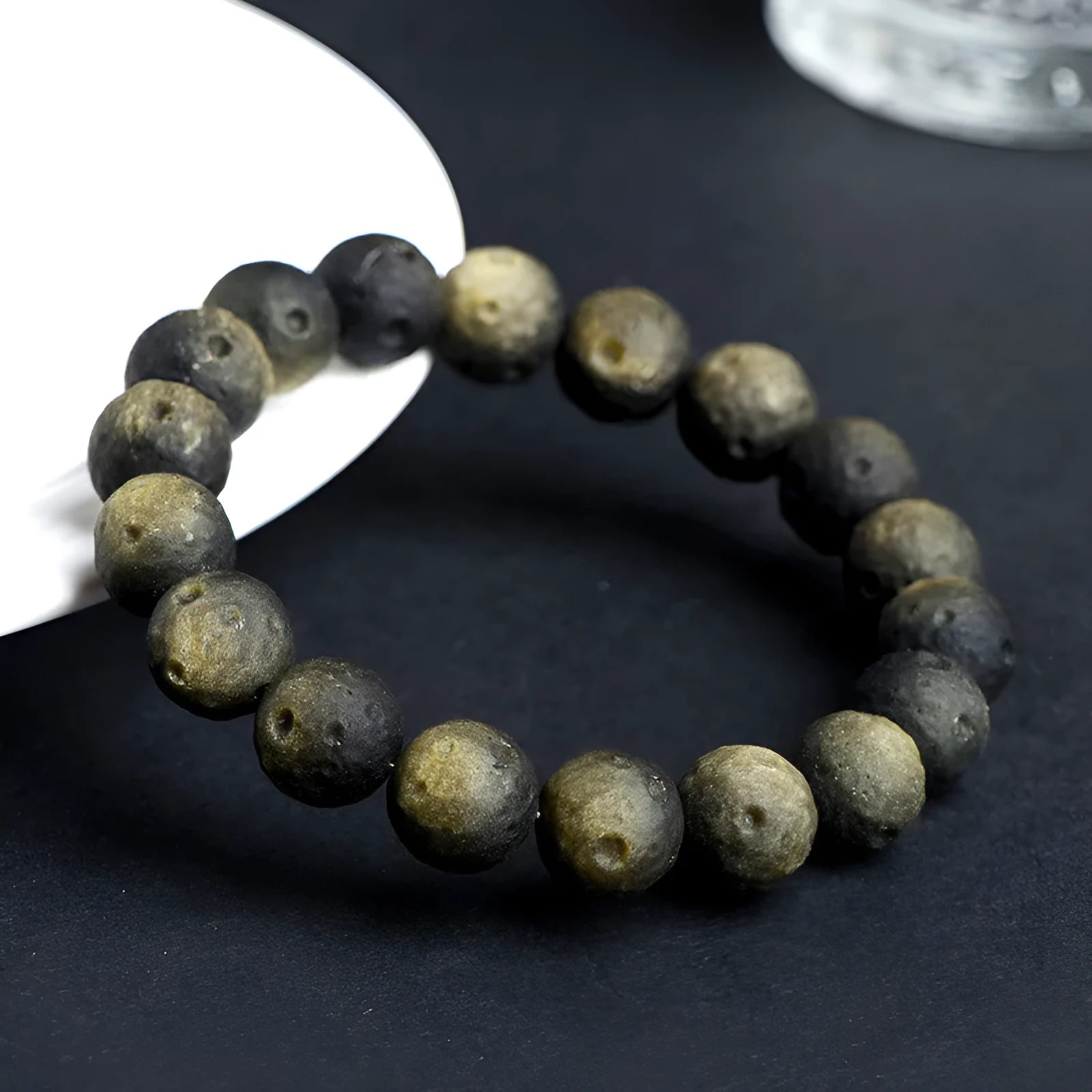Natural obsidian crater ball bracelet with meteorite-like texture in silver stone or gold finish.