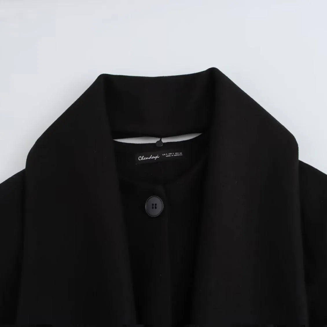 Women's long black polyester winter coat with a fluffy artificial fur collar, shown in a street fashion style.