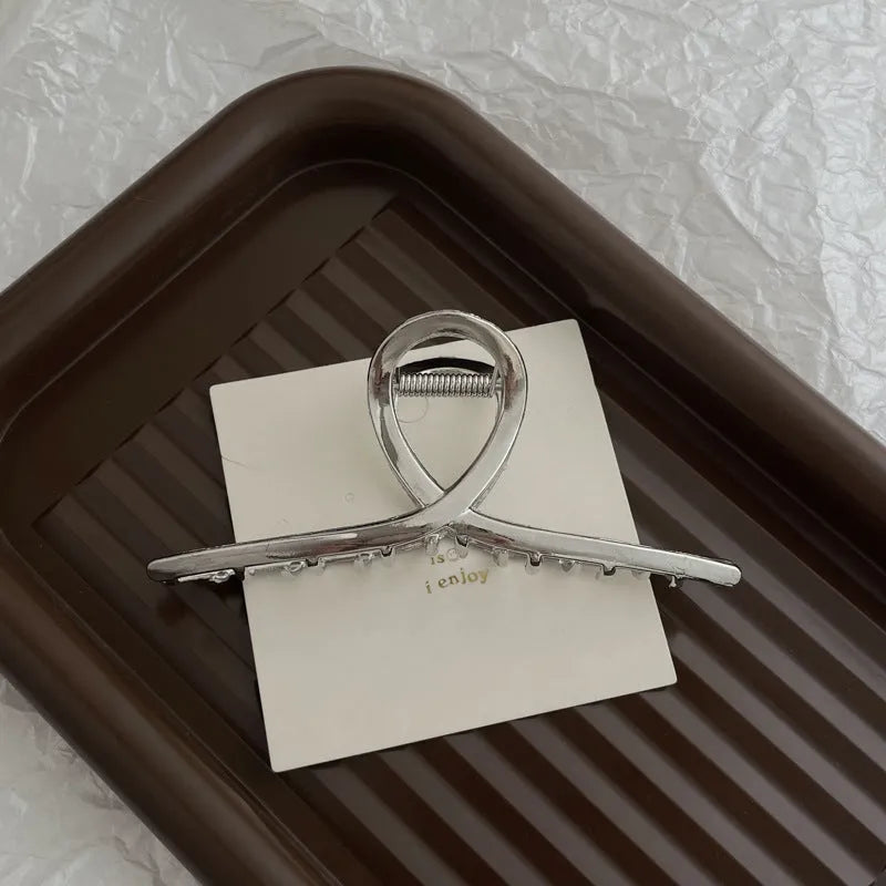 Assorted silver metal hair claws and barrettes including wave, knot, bow, and pearl designs on a white background.