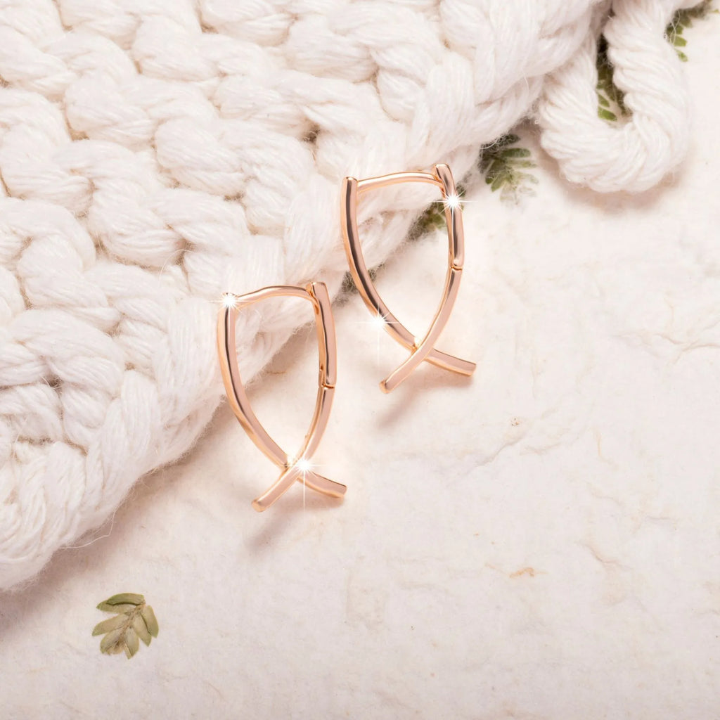 A pair of rose gold finished copper cross shaped drop earrings on a plain background.