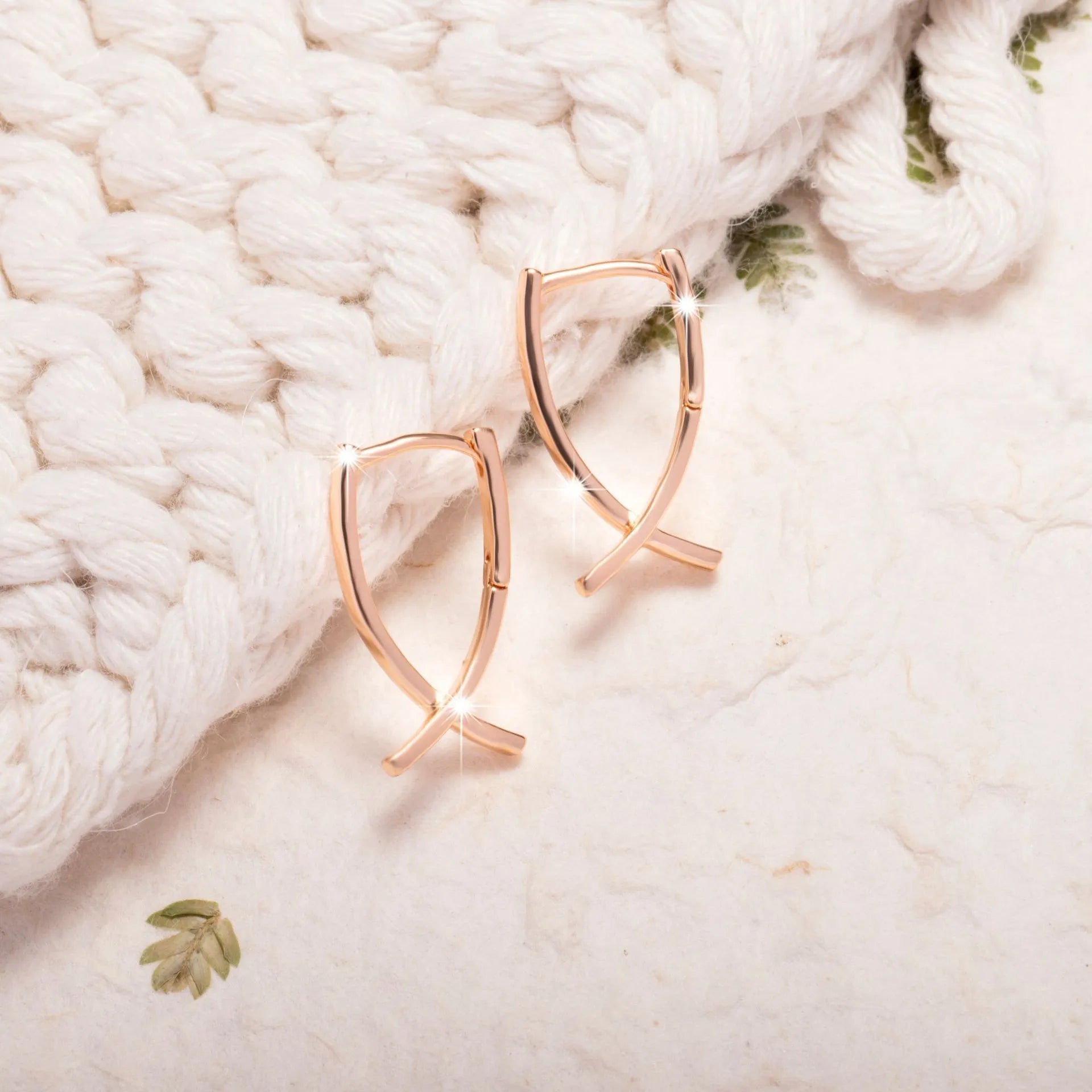 A pair of rose gold finished copper cross shaped drop earrings on a plain background.