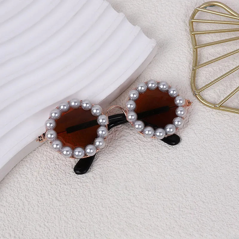 Pearl-rimmed round sunglasses for cats and dogs in multiple colours on a pink background.