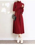 A rose red turtleneck knit dress with long sleeves, an elastic waist, and a loose mid-length skirt on a hanger.