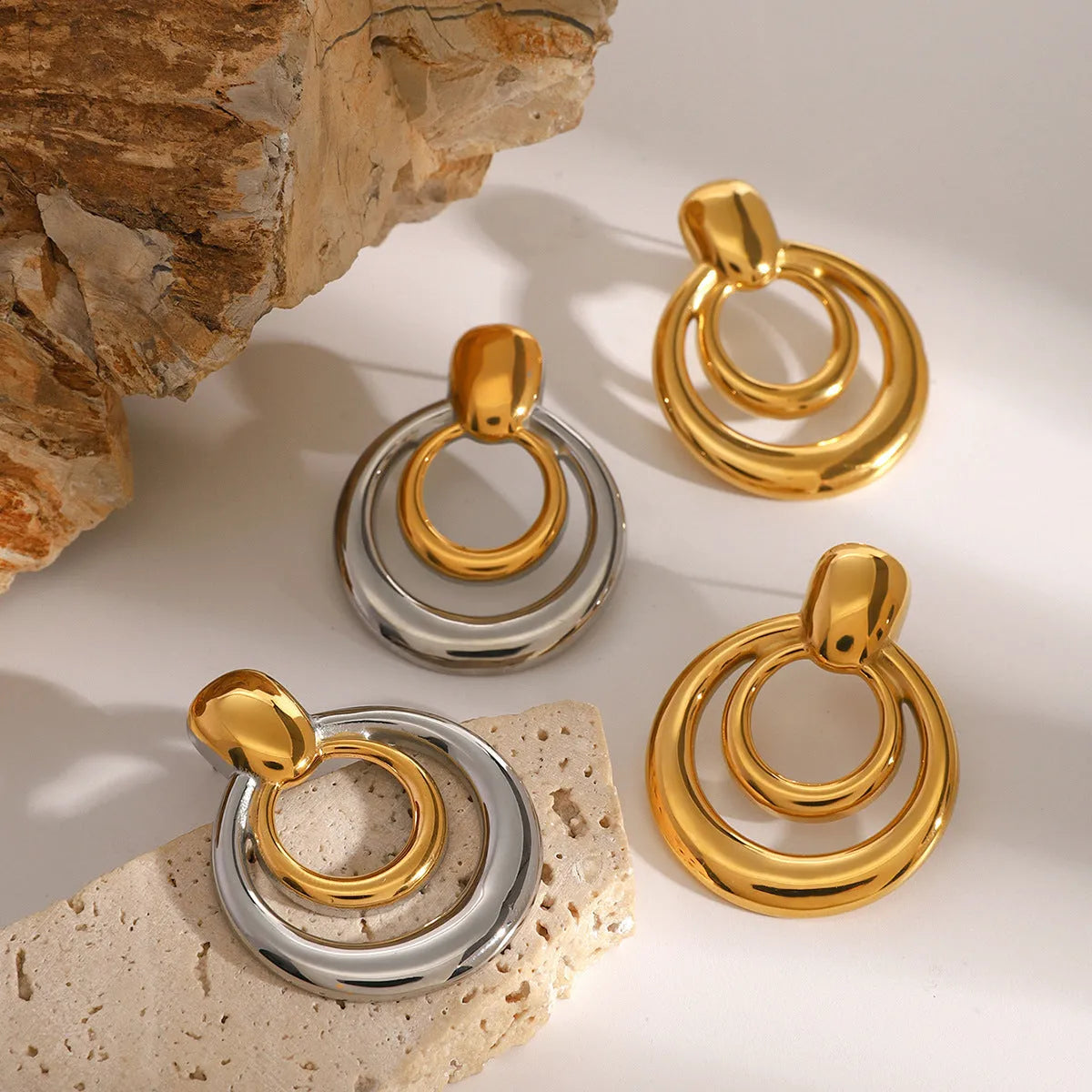 Close-up of a pair of round, geometric, double-layer hollow stud earrings with a golden electroplated finish.