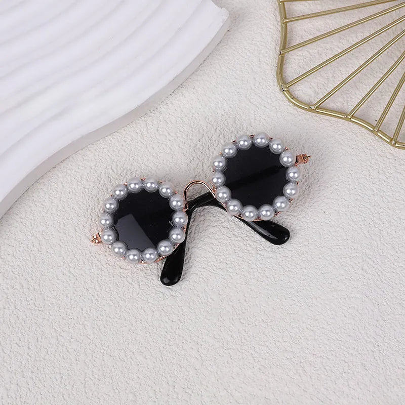 Pearl-rimmed round sunglasses for cats and dogs in multiple colours on a pink background.