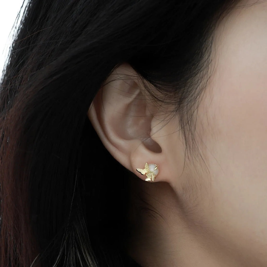 Close-up of a pair of silver butterfly stud earrings with a gold-toned finish.