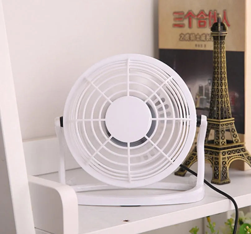 Mini black USB desk fan with adjustable head on a wooden desk next to a laptop.