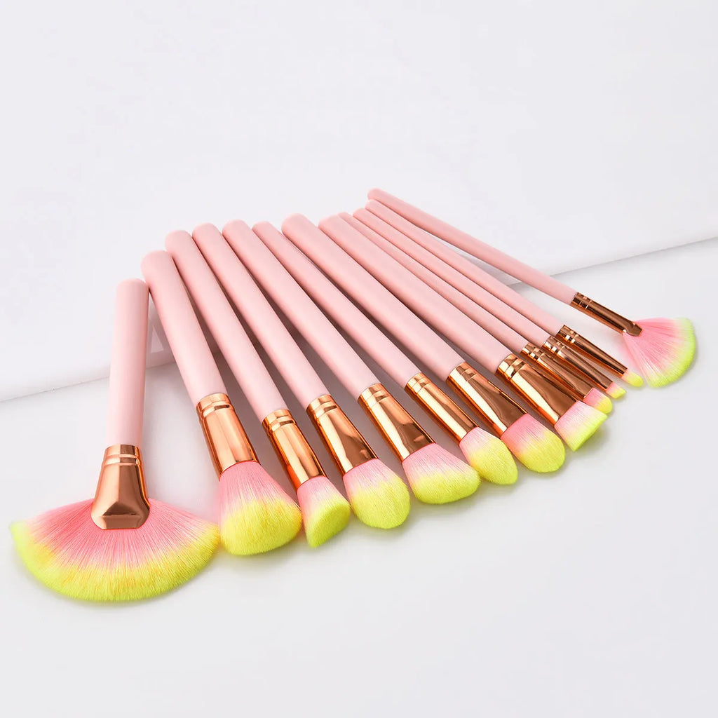 Twelve pink makeup brushes with nylon bristles and wood handles laid out in a row on a light background