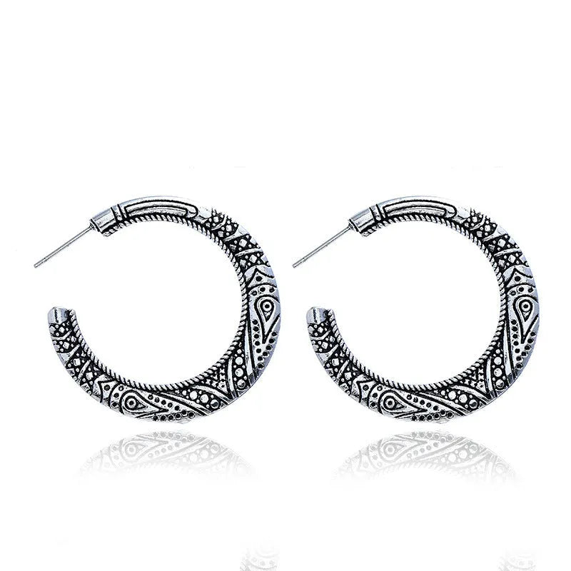 Pair of vintage engraved C-shaped alloy earrings in bronze on a plain background.