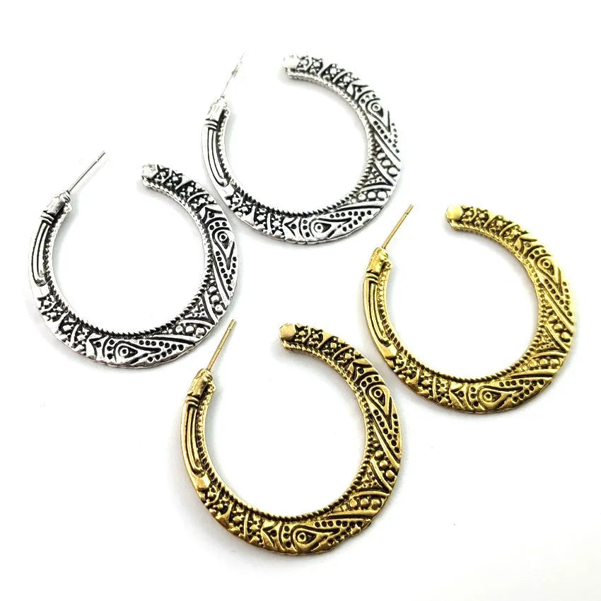 Pair of vintage engraved C-shaped alloy earrings in bronze on a plain background.