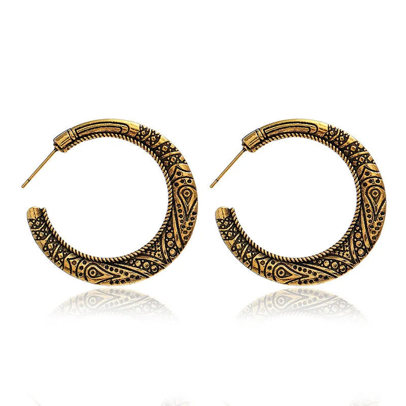 Pair of vintage engraved C-shaped alloy earrings in bronze on a plain background.