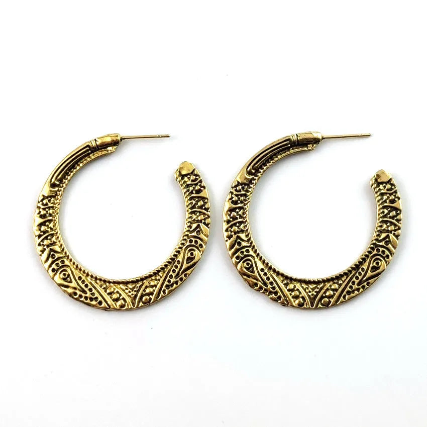 Pair of vintage engraved C-shaped alloy earrings in bronze on a plain background.