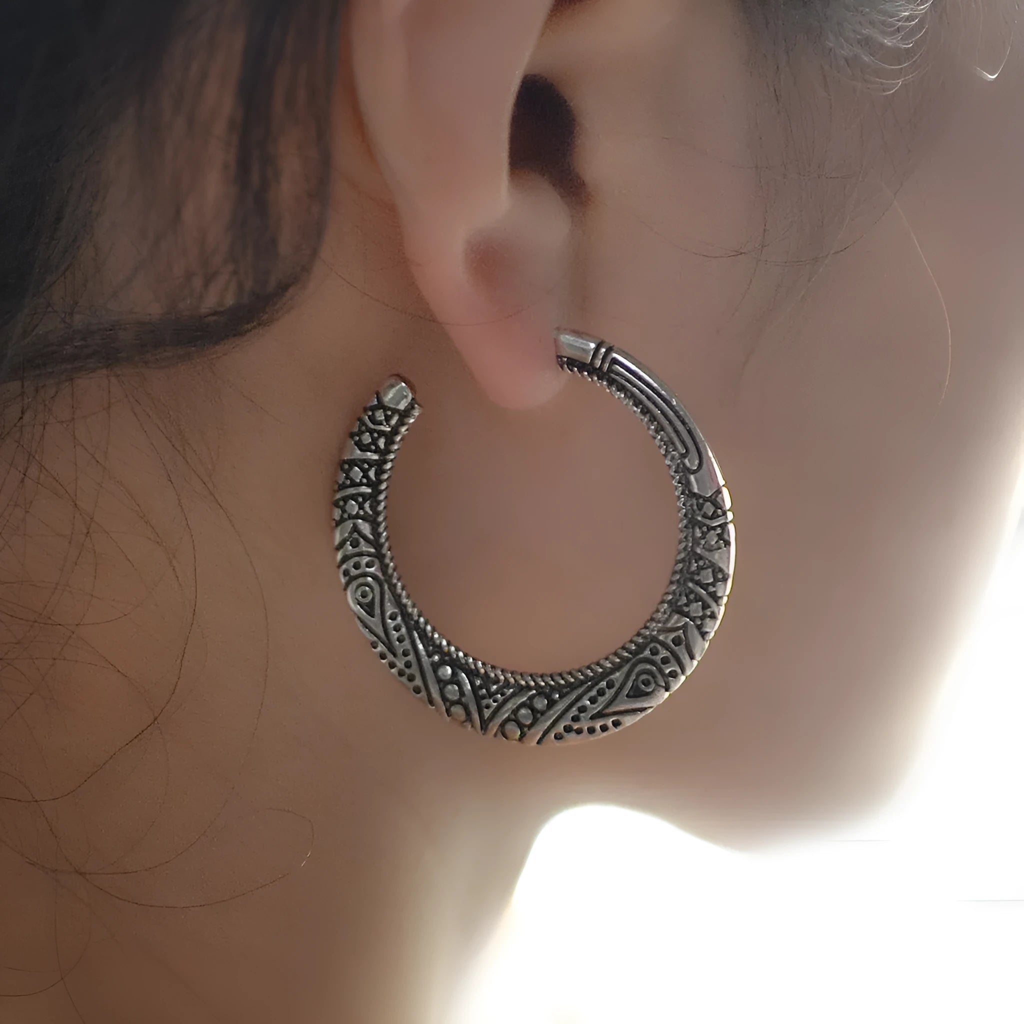Pair of vintage engraved C-shaped alloy earrings in bronze on a plain background.