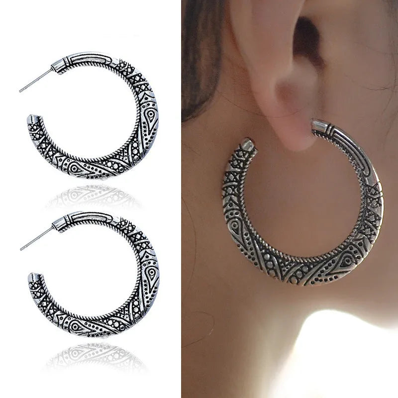 Pair of vintage engraved C-shaped alloy earrings in bronze on a plain background.