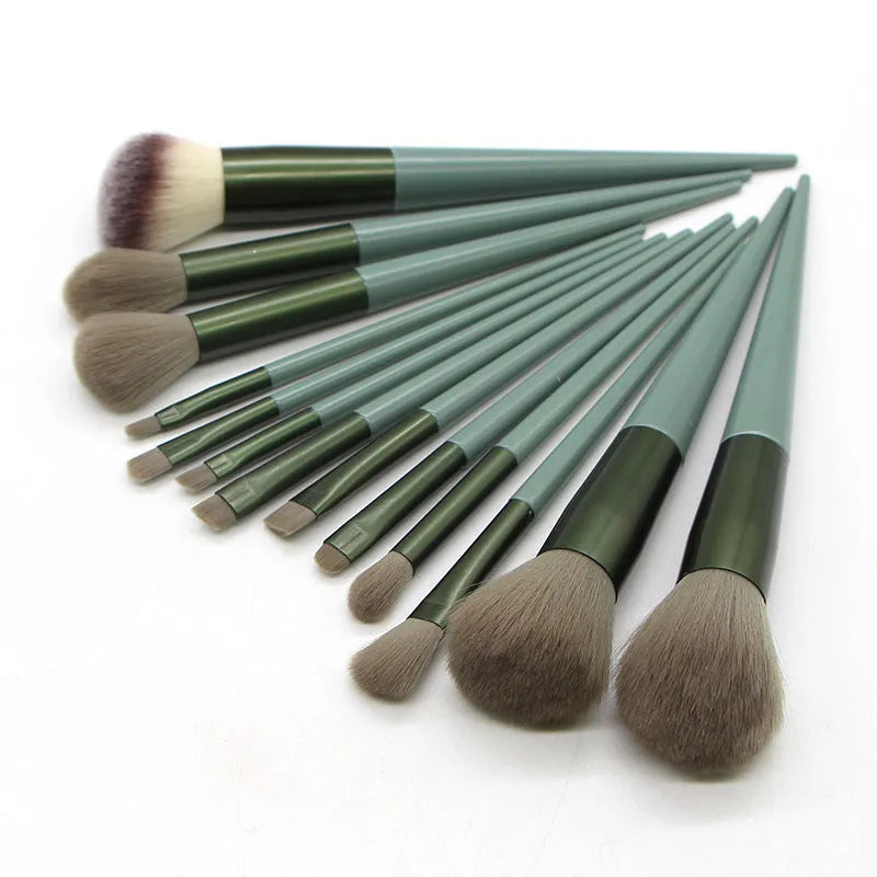13 green makeup brushes with fibre wool bristles and aluminium tubes arranged on a surface