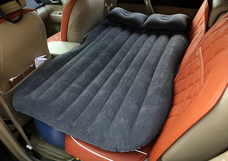 Black inflatable car bed with flocked surface set up in the back of a five-seater vehicle with pillows.
