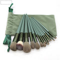 13 green makeup brushes with fibre wool bristles and aluminium tubes arranged on a surface