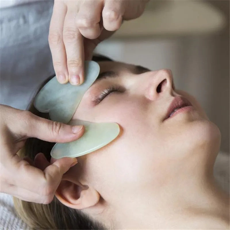 Natural jade gua sha scraper in heart shape on a light surface, 6.3cm x 4.5cm, hand-polished stone