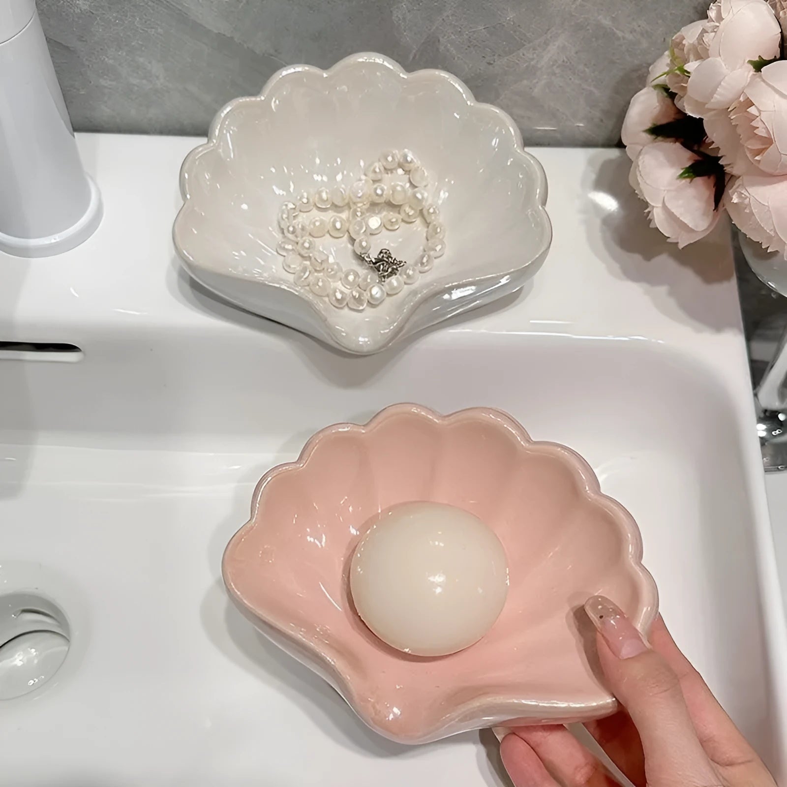 White or pink plastic shell-shaped soap dish with slatted base for bathroom use.