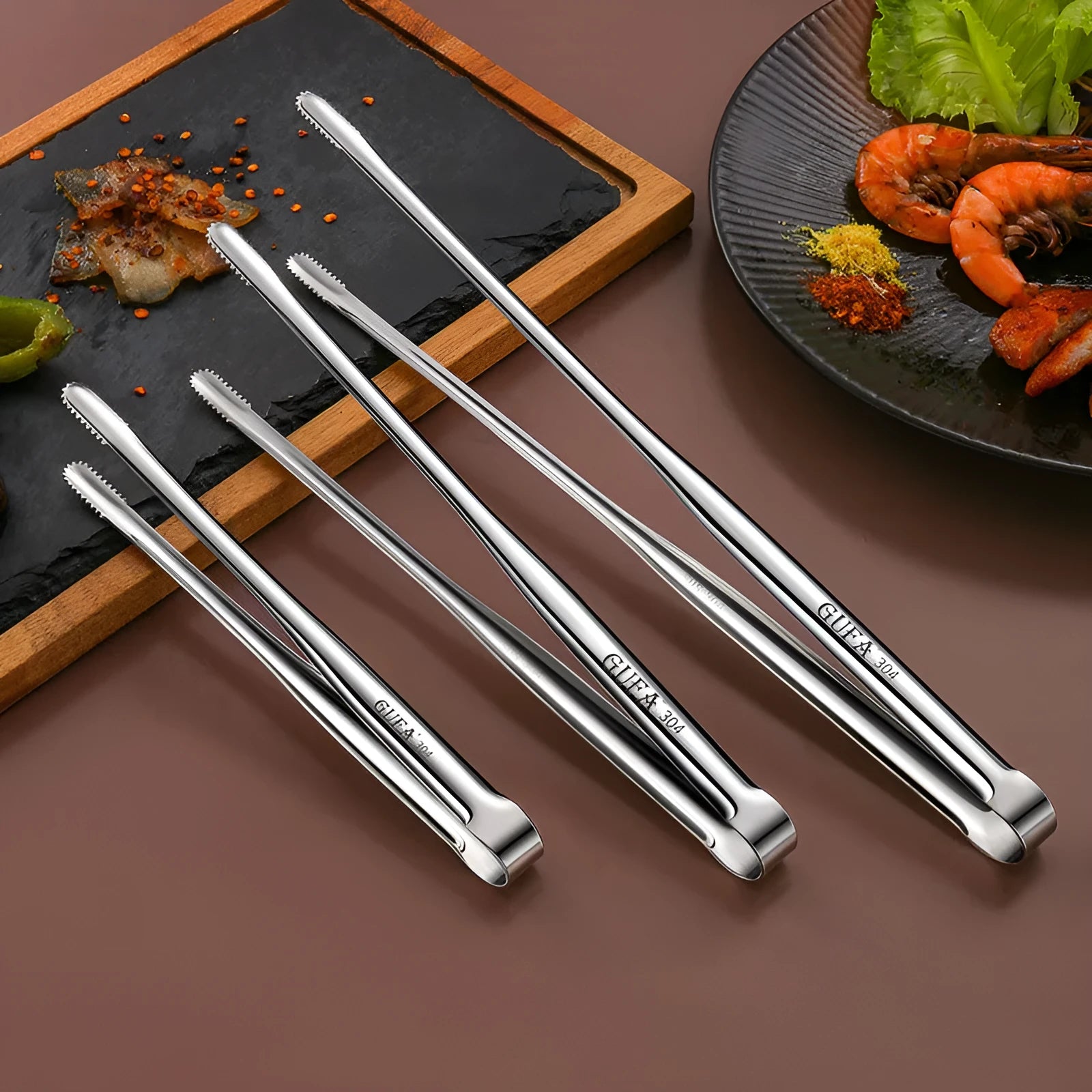 Stainless steel barbecue clamp in modern simple design on a table, showing the three size options small medium large