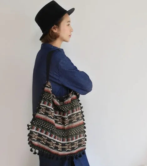 Green geometric tribal tasselled tote bag with oval shape, open top, and two handles, shown on a flat surface