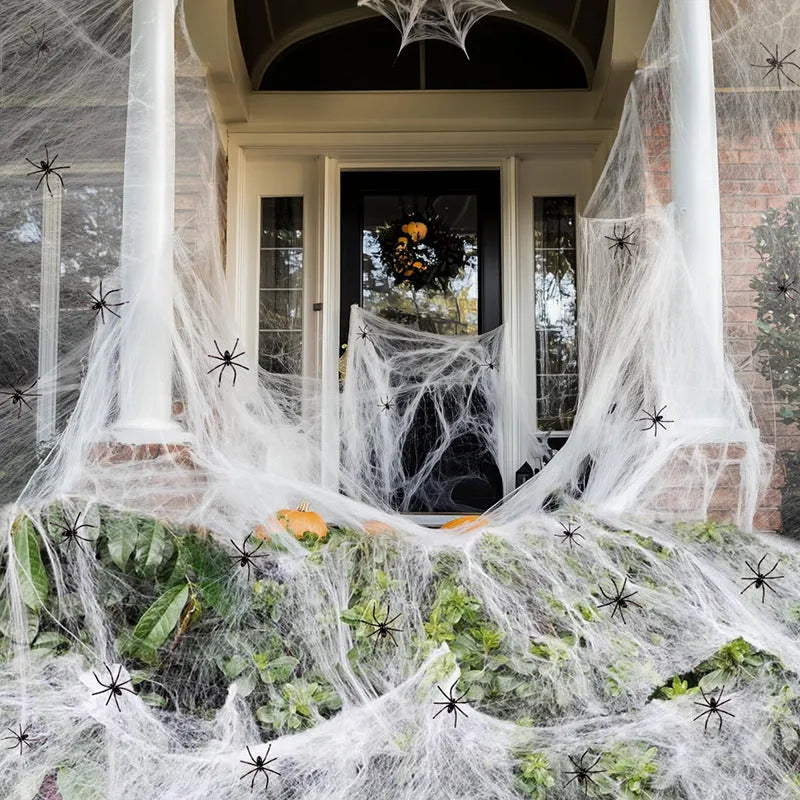White cotton spider web Halloween decoration draped over a branch with plastic spiders.