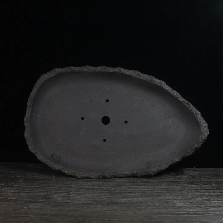 Handmade purple clay flowerpot in a unique shape, shown on floor beside a plant.