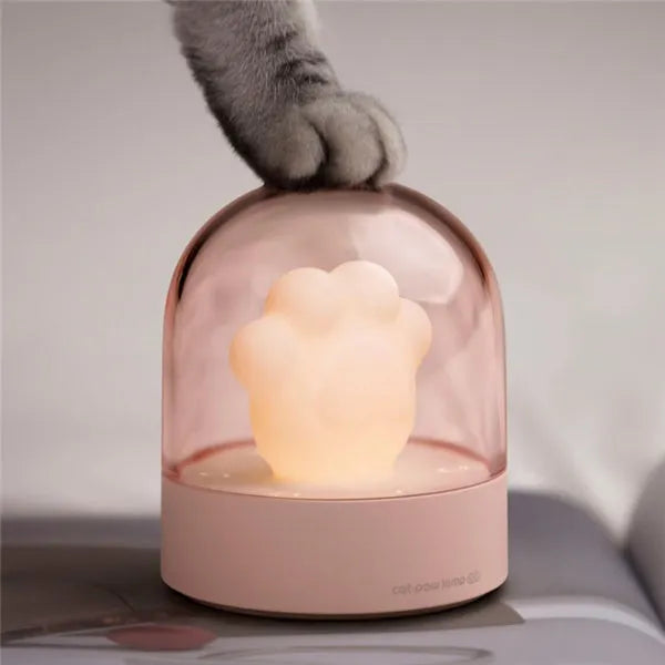 Grey or pink cat paw shaped USB rechargeable night light and music box on a desktop.