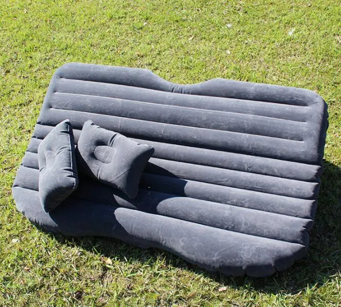 Black inflatable car bed with flocked surface set up in the back of a five-seater vehicle with pillows.