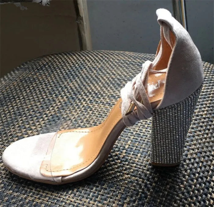 A pair of women's black plastic high heel sandals with a pointed toe on a plain background.