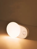 White Baseus rechargeable sensor night light with LED glow on a bedside table.