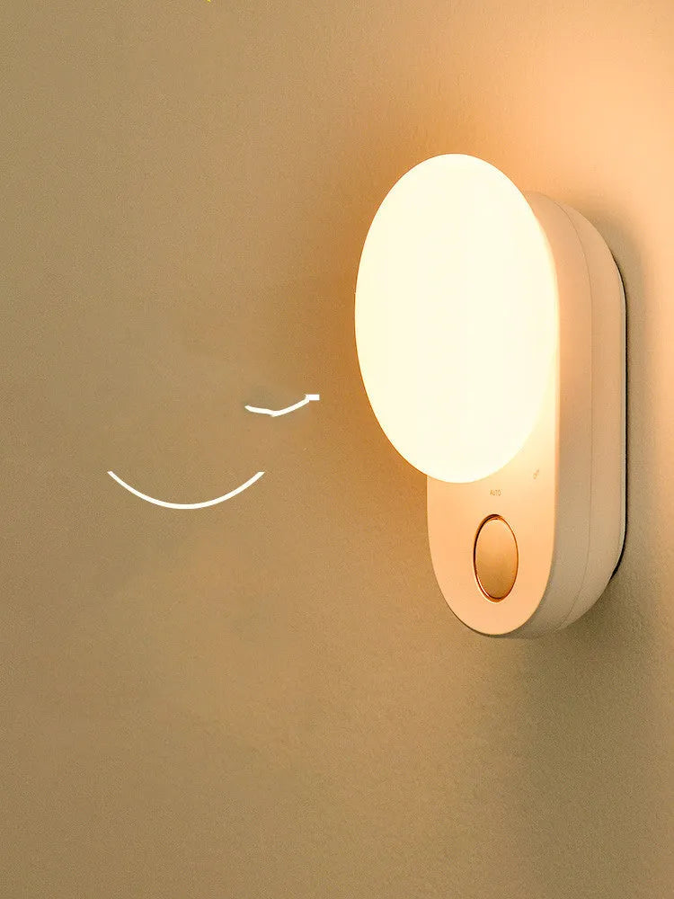 White Baseus rechargeable sensor night light with LED glow on a bedside table.