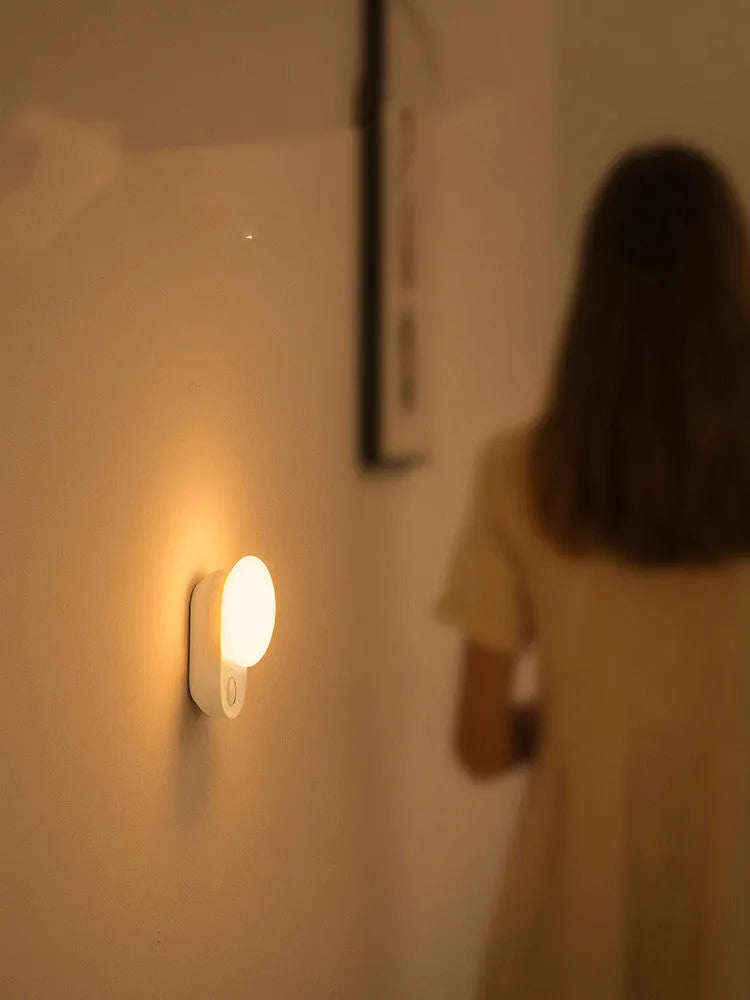 White Baseus rechargeable sensor night light with LED glow on a bedside table.
