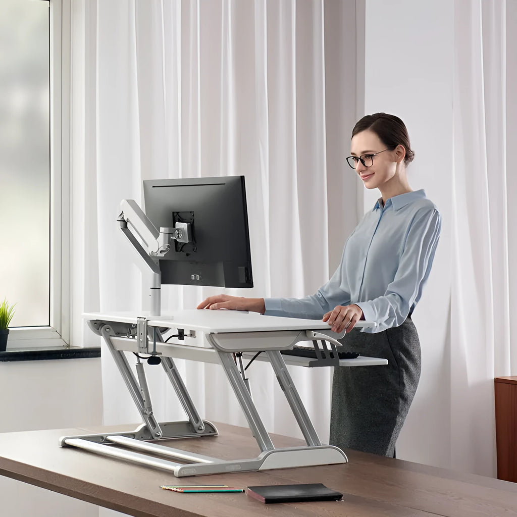 Lifting computer stand in dark grey with a monitor placed on top, shown on a desk for ergonomic viewing height.