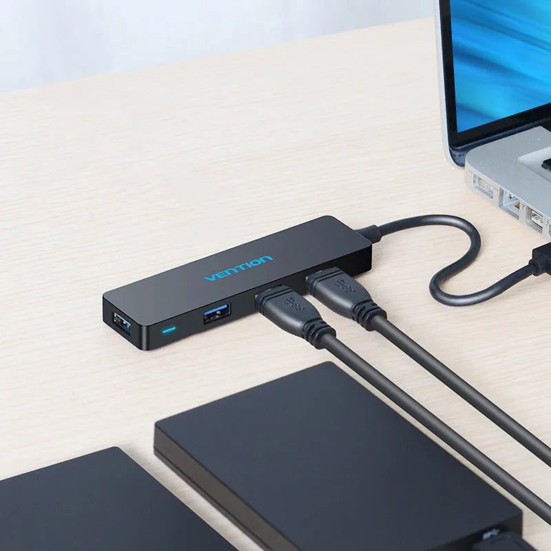 Black four-port USB 3.0 hub with a short cable next to a laptop