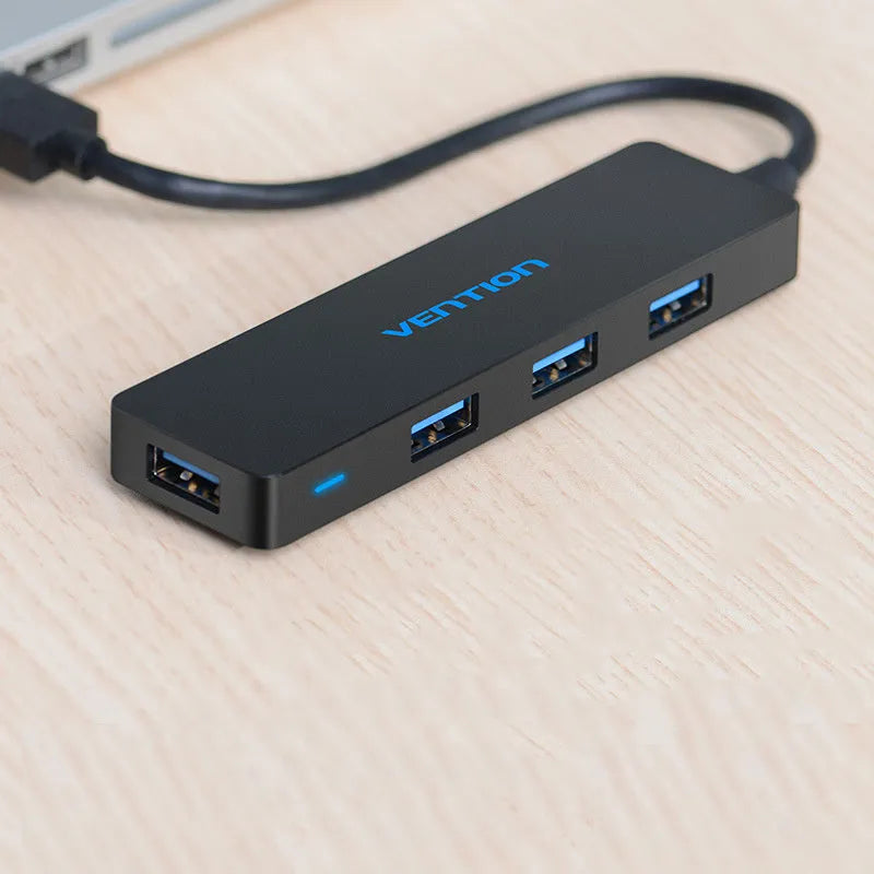 Black four-port USB 3.0 hub with a short cable next to a laptop