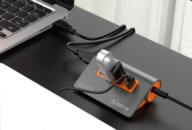 Dark grey USB hub with four ports and orange accents, showing aluminium construction and separate data cable
