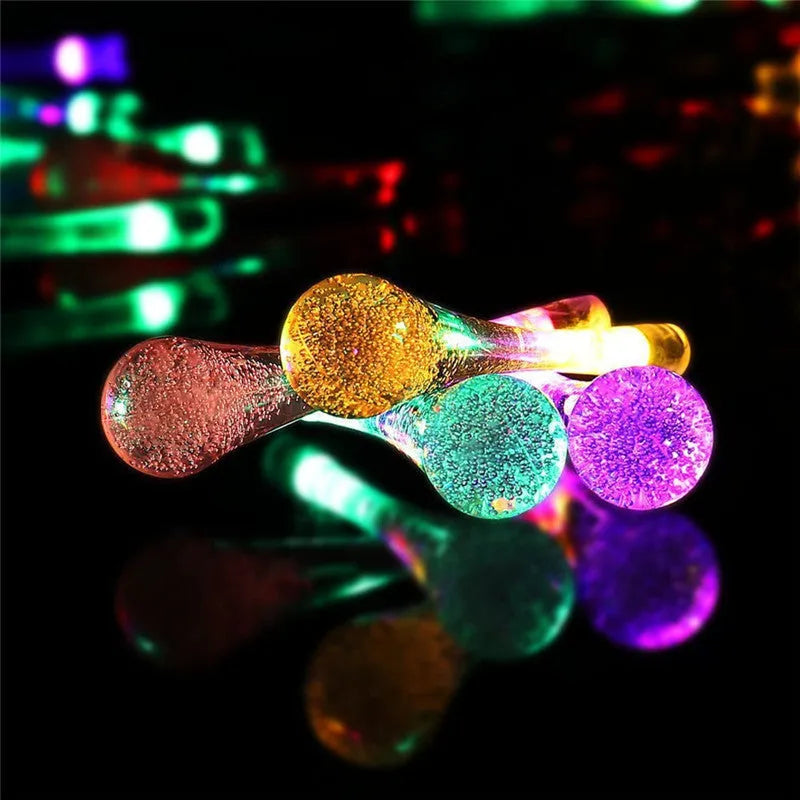 Solar-powered outdoor string lights with water drop shaped pendants on a 6.5 metre cable, shown with solar panel and ground spike.