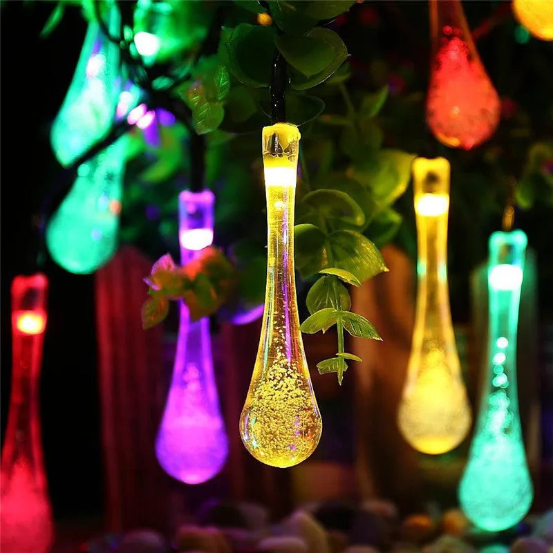 Solar-powered outdoor string lights with water drop shaped pendants on a 6.5 metre cable, shown with solar panel and ground spike.