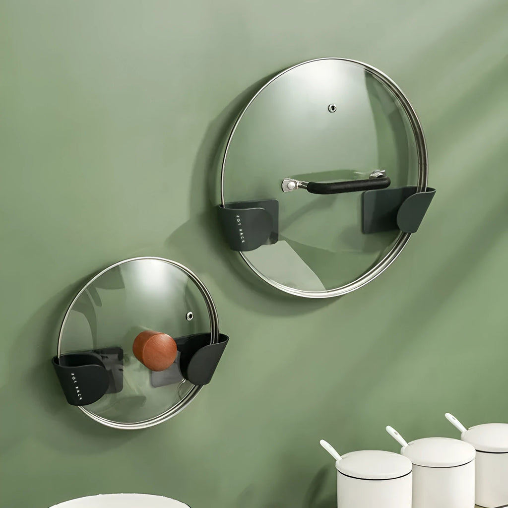Black pot cover rack wall-mounted on white tile holding a metal saucepan lid
