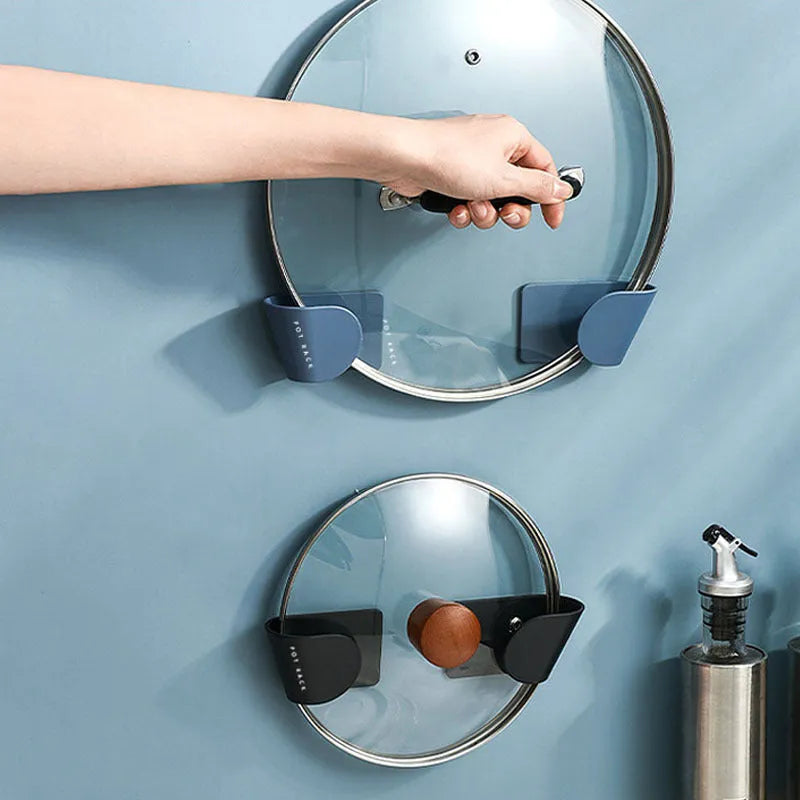 Black pot cover rack wall-mounted on white tile holding a metal saucepan lid