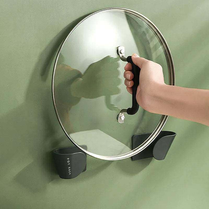 Black pot cover rack wall-mounted on white tile holding a metal saucepan lid