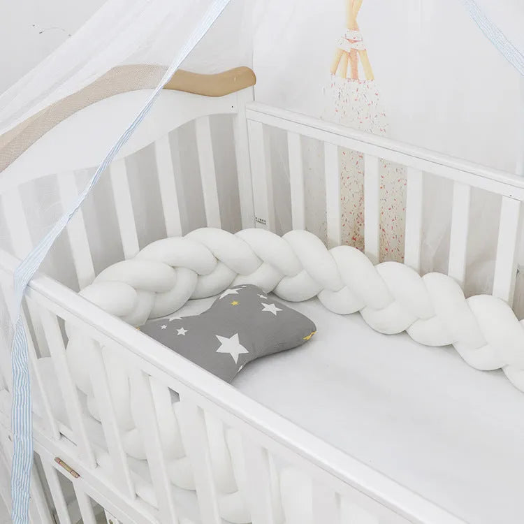 Braided knot crib bumper in spandex velvet, shown bending to fit a white wooden cot.