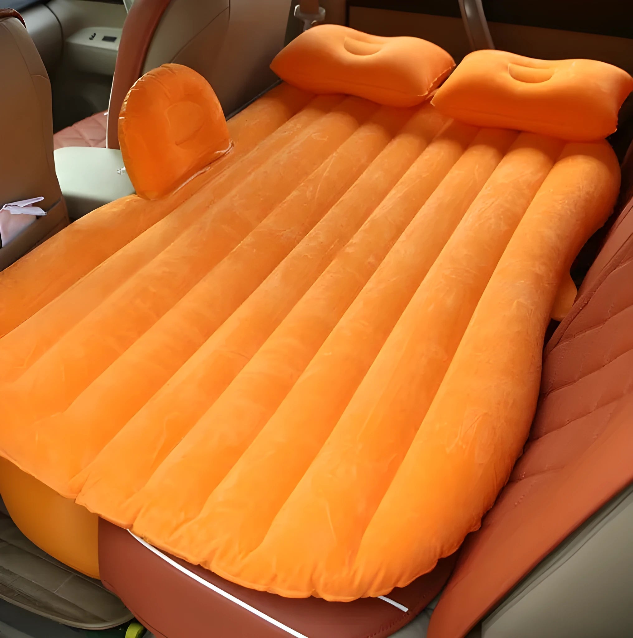 Black inflatable car bed with flocked surface set up in the back of a five-seater vehicle with pillows.