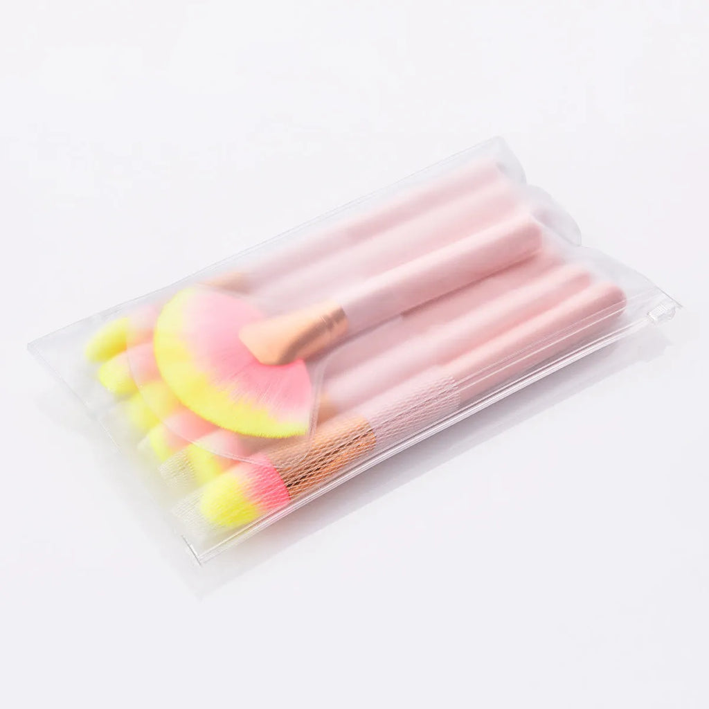 Twelve pink makeup brushes with nylon bristles and wood handles laid out in a row on a light background