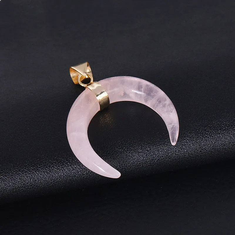 Close-up of a moon pendant necklace with a pink natural stone, on a copper-coloured chain against a neutral background.