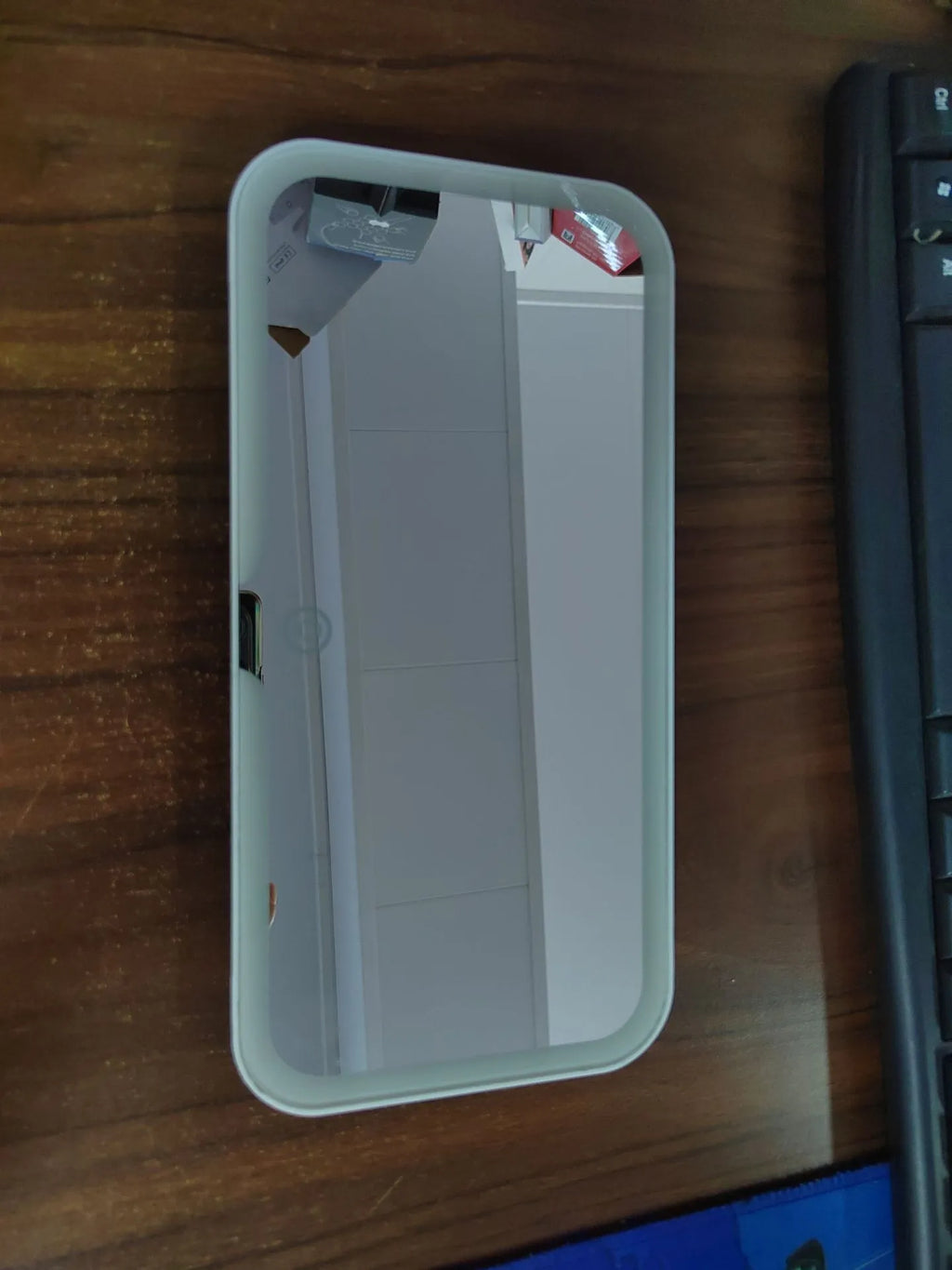 White car sun visor with LED make-up mirror showing illuminated reflection on aluminium surface