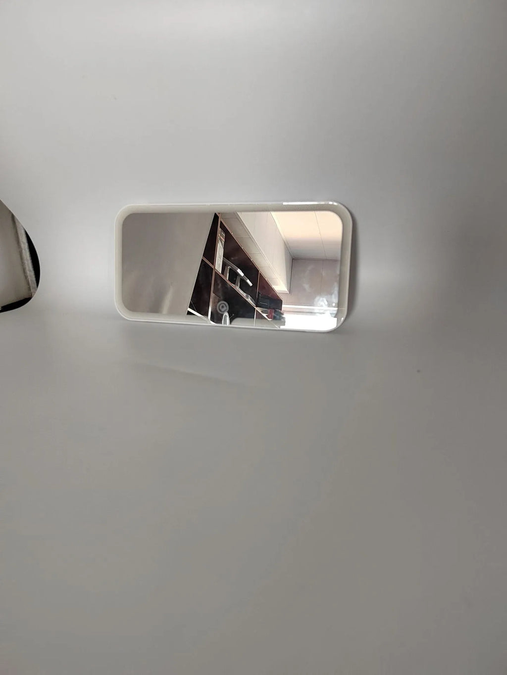 White car sun visor with LED make-up mirror showing illuminated reflection on aluminium surface