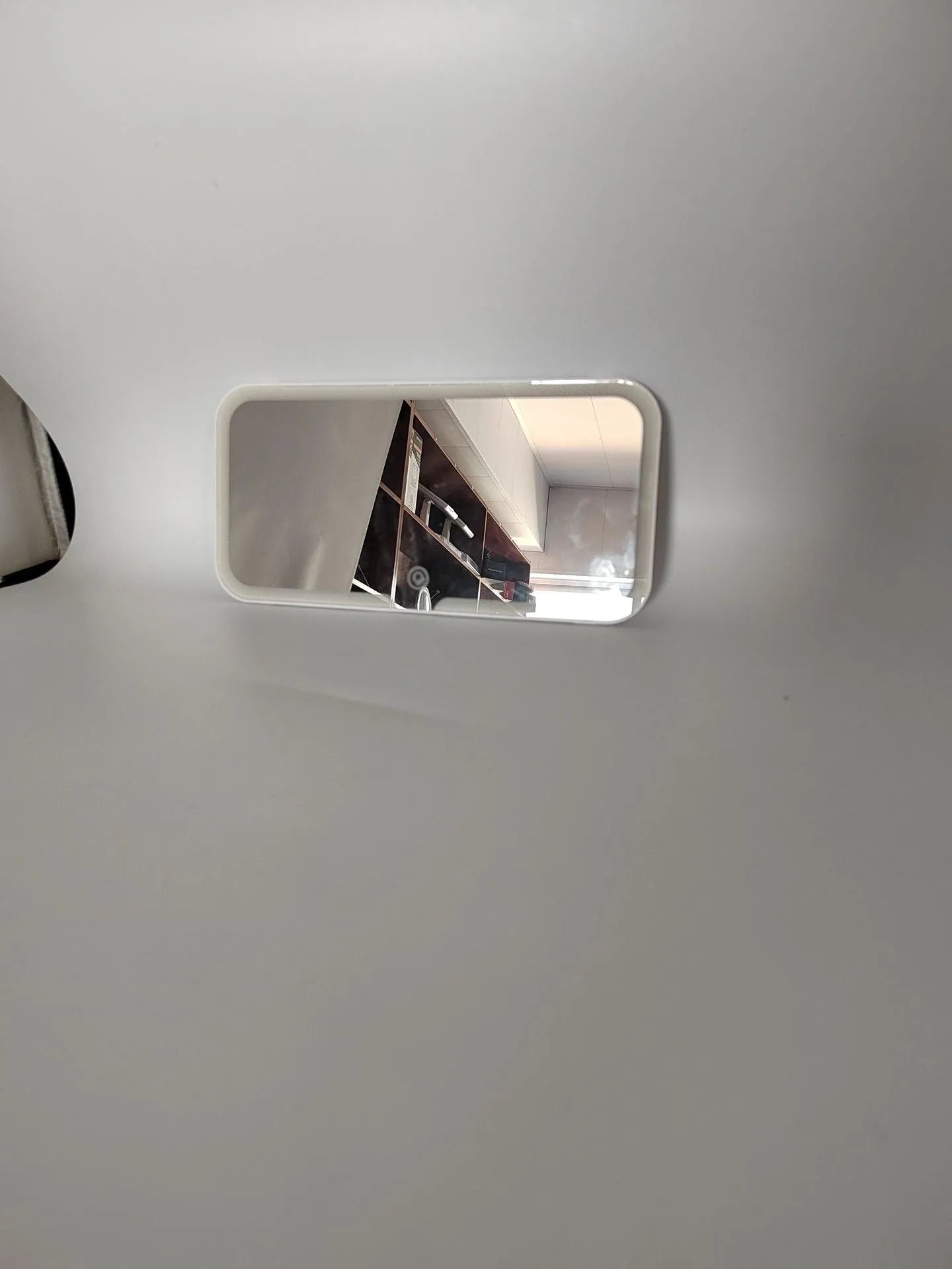 White car sun visor with LED make-up mirror showing illuminated reflection on aluminium surface